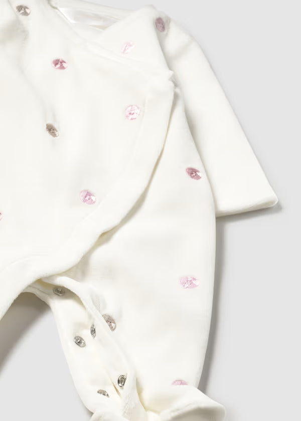 Tutina ciniglia bianca neonata con bottoni a pressione e applicazioni decorative rosa e grigie.