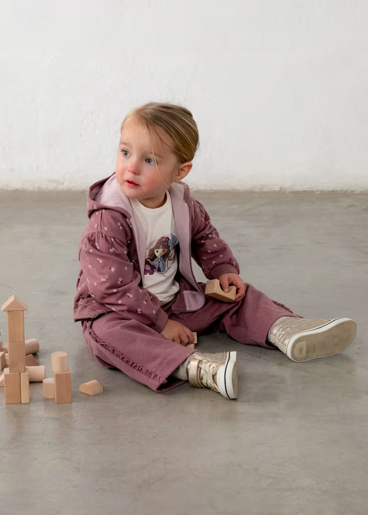 TUTA 3PZ BAMBOLA composta da felpa con cappuccio e pantaloni rosa, t-shirt bianca con stampa bambola e scarpe beige.